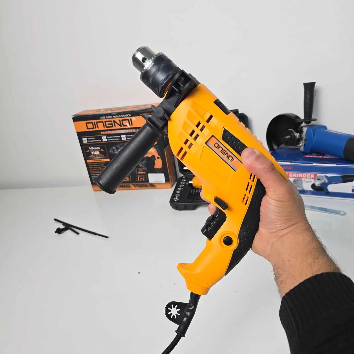 Hand holding yellow Dingqi electric impact drill with black handle and drill box in background on white surface
