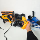 Hand holding yellow QINGNQ heat gun with impact drill and angle grinder tools on white surface